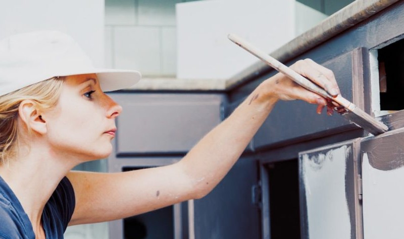 young woman holding a brush coloring a kitchen cabinet