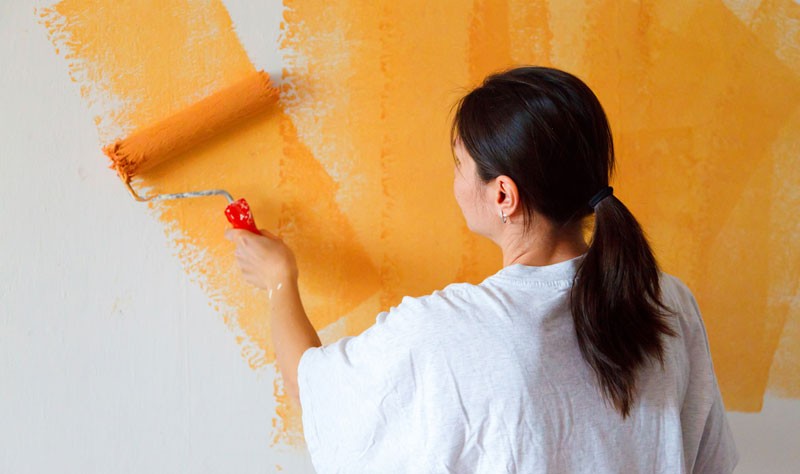 young woman holding a paint brush coloring a wall