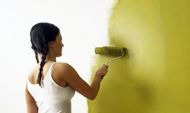 young woman coloring a wall with a roller brush